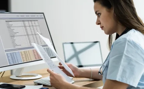 person in front of computer with medical bill codes and spreadsheets