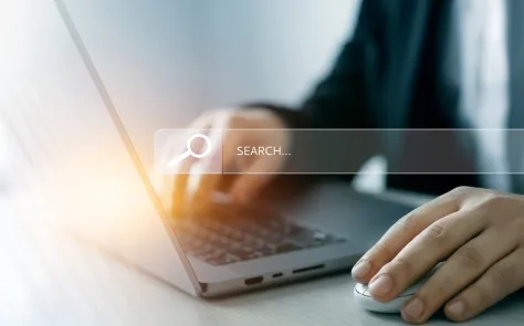 Person using a laptop and mouse with a search bar overlay, representing website navigation.