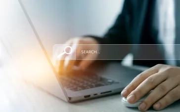 Person using a laptop and mouse with a search bar overlay, representing website navigation.